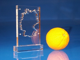 Award in mit gelaserter Deutschlandkarten-Kontur, auf Sockel verklebt. Eine Orange als Größenvergleich daneben.